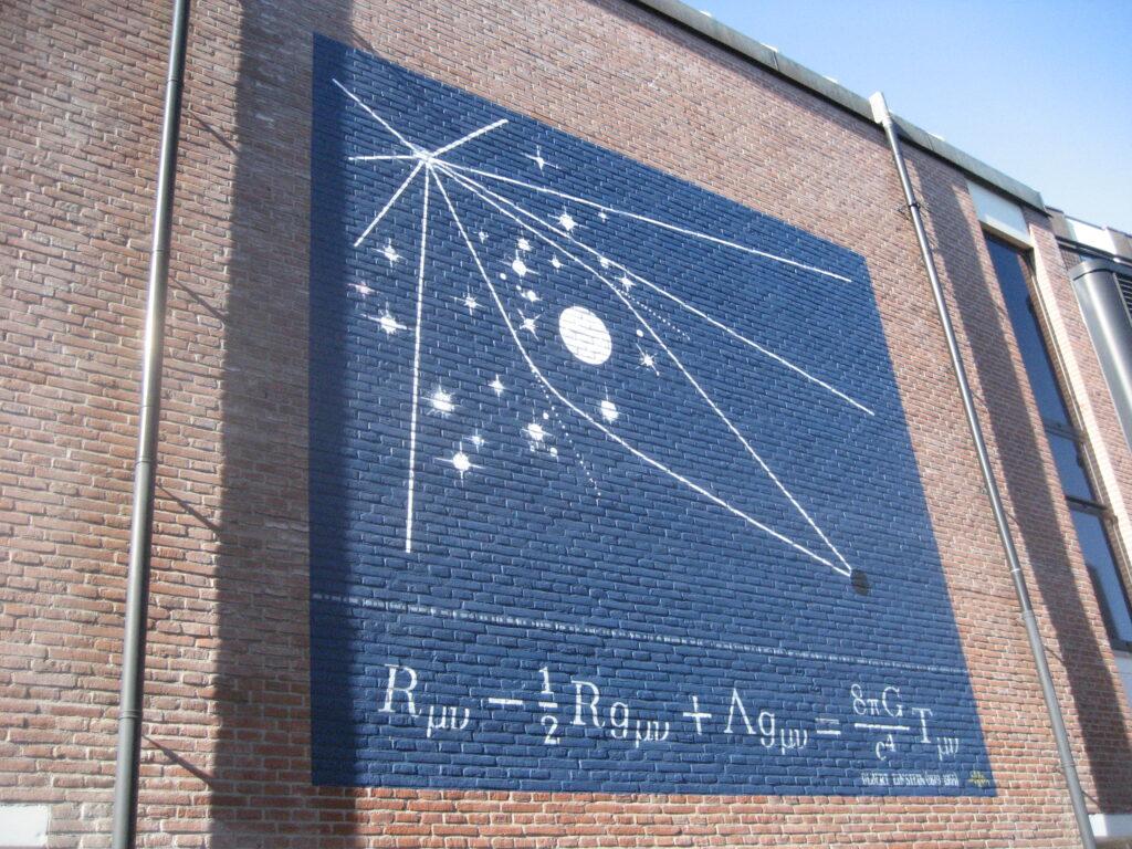 Mural de la calle Lange Sint Agnietenstraat, en la ciudad de Leiden en Países Bajos, que exhibe un diagrama de lente gravitacional y la famosa ecuación de Einstein de la relatividad general. 